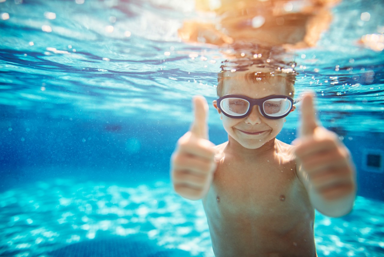 6岁的小男孩在水下游泳。男孩对着镜头微笑，竖起大拇指。